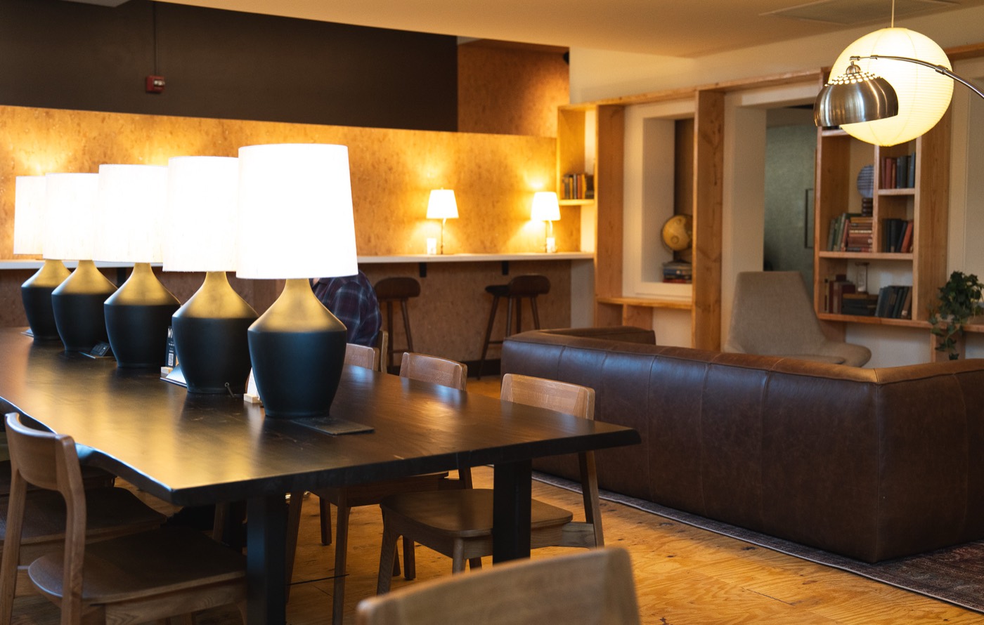 The lounge at The Work Club, with lamps along a long work table and a leather sofa