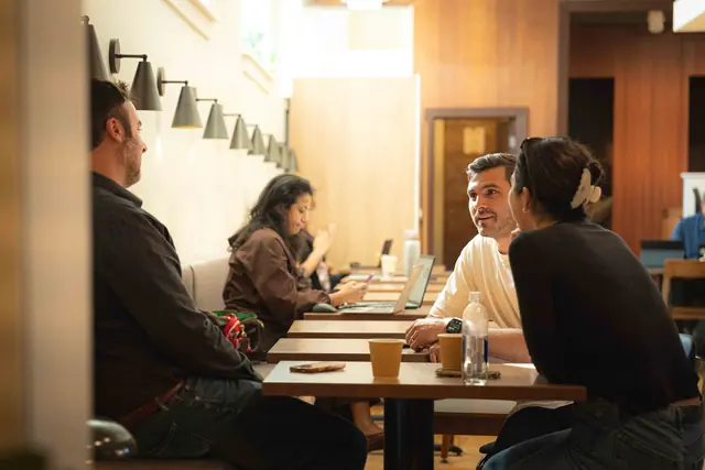 Two members talking over coffee at a long table at The Work Club